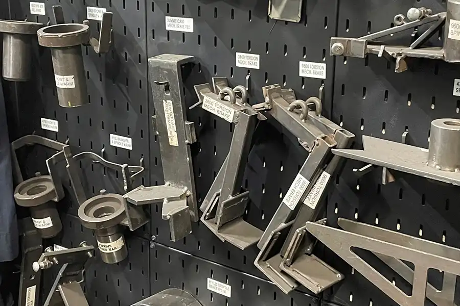 A black pegboard wall with various labeled metal fixtures and tools hanging from hooks, each with white identification tags—demonstrating the organization and clarity found in the 5 Key Features of a 5S Workstation within a workshop or industrial setting.